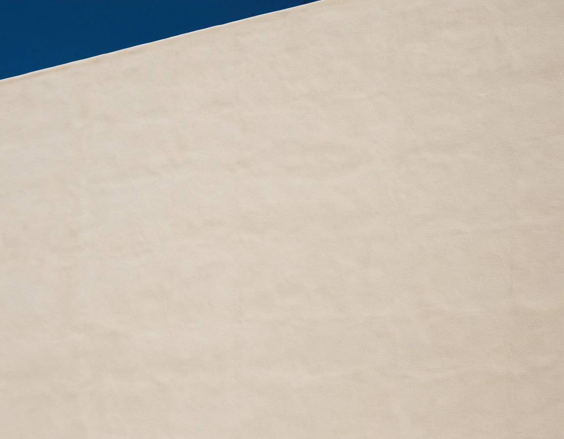 A white rendered villa wall in strong sunlight with a straight vertical movement joint casting a thin shadow.